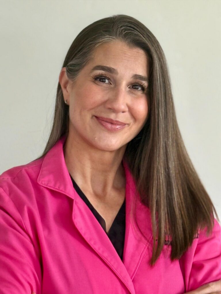 A woman in a pink coat smiling at the camera against an off white background.